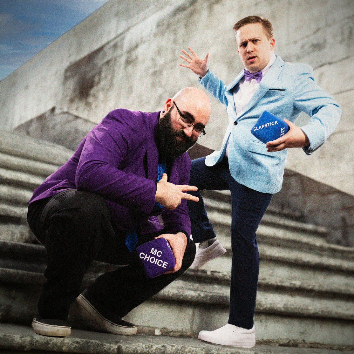 Josh and Milan posing on concrete steps with the genre and punchline dice